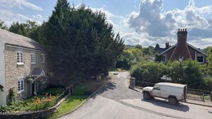 Eine ländliche Straße mit einem weißen Lieferwagen, der am Rand geparkt ist, umgeben von Steinbauten und Grünpflanzen.
