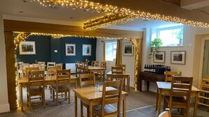 Ein Restaurantinneres mit mehreren Holztischen und -stühlen, Lichterketten, gerahmten Bildern an den Wänden und einem Weinregal.