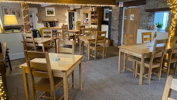 A cozy dining area with wooden tables and chairs, stone walls, and string lights.