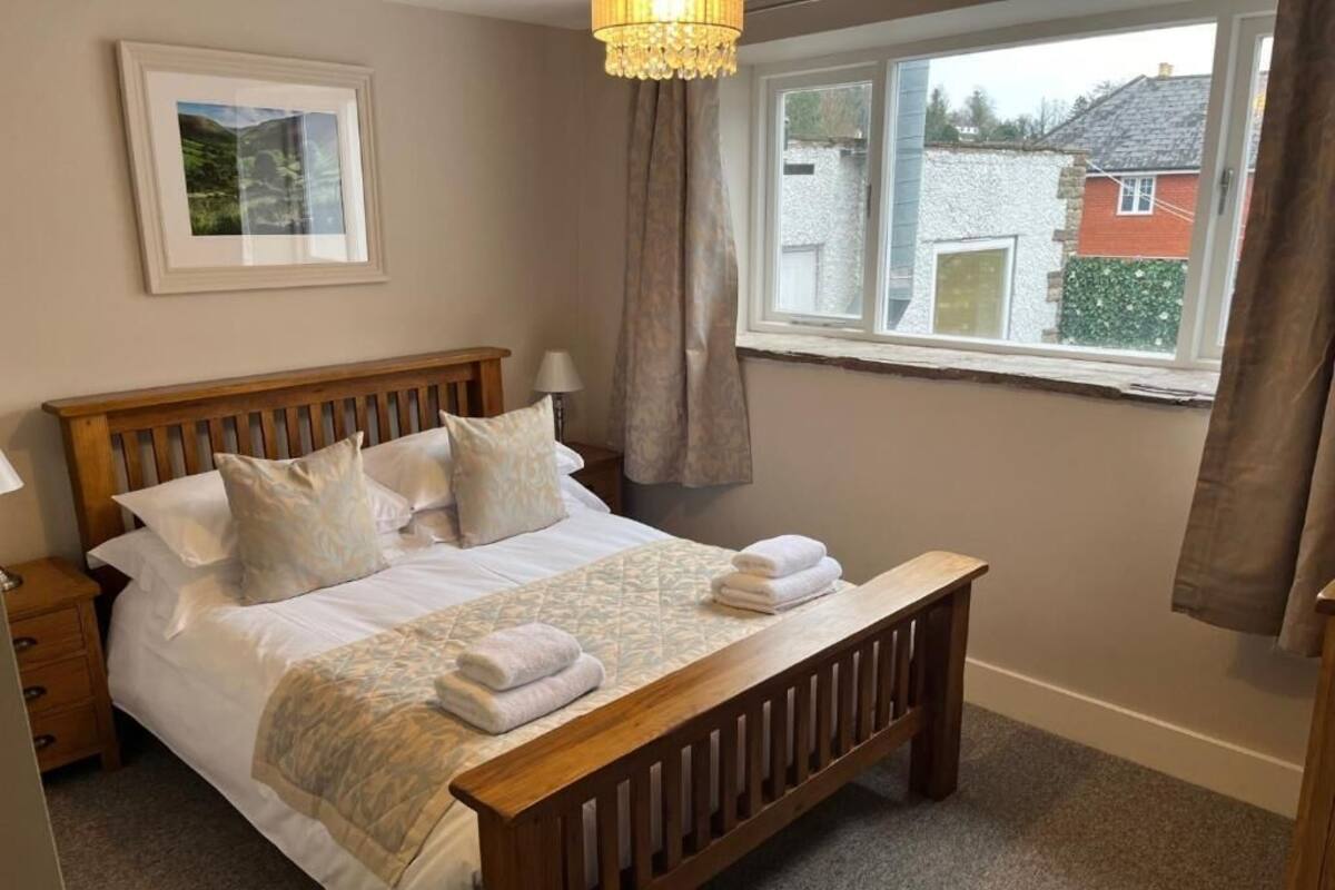 Un dormitorio con cama de madera, una mesita de noche, una ventana con cortinas y un cuadro en la pared.