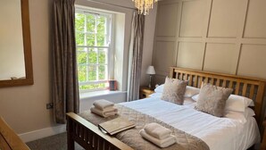 Ein Schlafzimmer mit einem hölzernen Bett, einem Nachttisch, Vorhängen an einem Fenster und einer Chandelier.