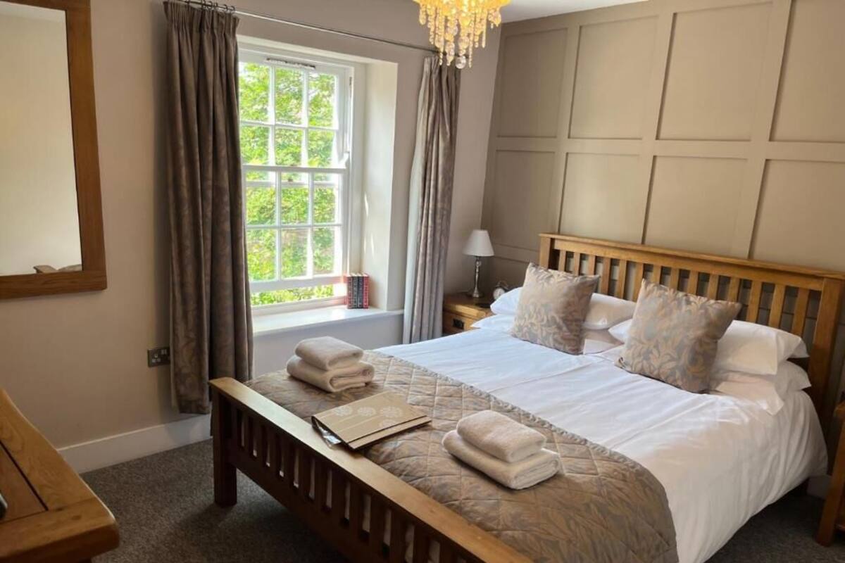 Un dormitorio con una cama de madera, una mesita de noche, cortinas en la ventana y un candelabro.