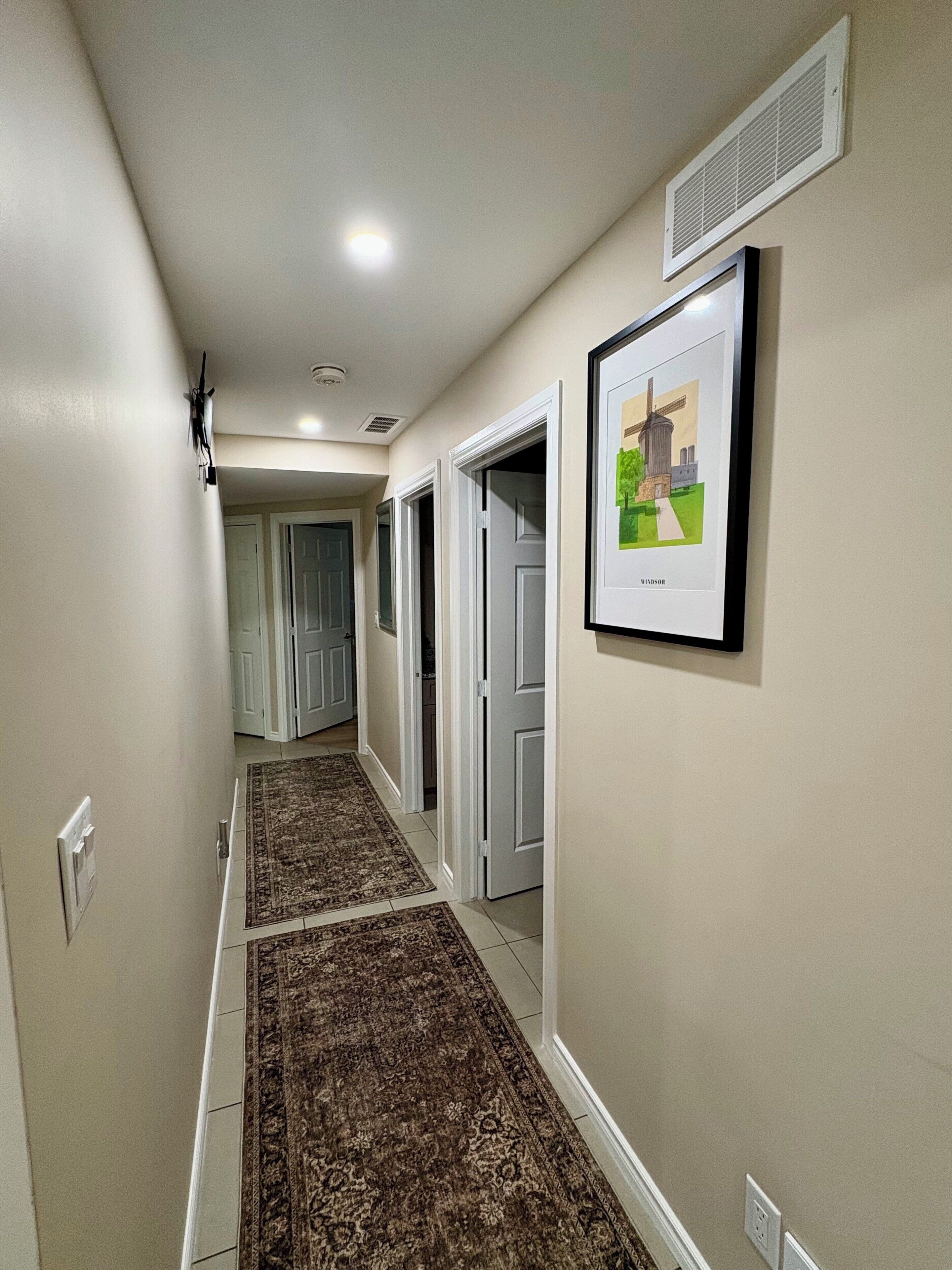 Un couloir avec un tapis à motifs, des portes blanches et un tableau encadré accroché au mur.