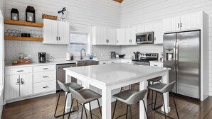 A modern kitchen with white cabinetry, a large island with bar stools, a stainless steel refrigerator, and a wooden ceiling. - Lakefront - Private Dock - Near Ark - Sleeps 14 (Williamstown)