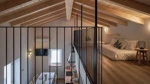 A loft bedroom with a sloped ceiling, a bed, a small table, and a staircase. - Historic 1940s Watermill: A Designer Retreat in the Italian Alps (Cerete Basso)
