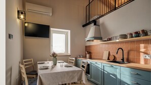 A kitchen with a dining table, chairs, a TV, and a window. - Historic 1940s Watermill: A Designer Retreat in the Italian Alps (Cerete Basso)
