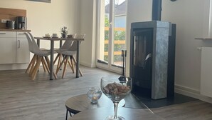 A modern kitchen with a dining area, a fireplace, and a large window. - Apartment Kaiserperle at Haus Urvasi - Seaside-Flair with sauna and fireplace (Lübeck)