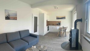 A modern living room with a sofa, a dining table, and a kitchen area in the background. - Apartment Kaiserperle at Haus Urvasi - Seaside-Flair with sauna and fireplace (Lübeck)