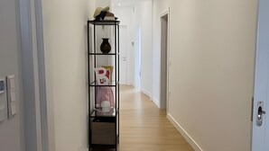 Ein Flur mit Holzboden, weißen Wänden und einer schwarzen Regaleinheit mit diversen Gegenständen.