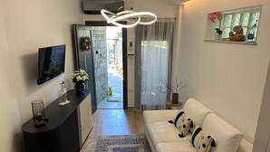 Un saló modern amb un sofà, una taula baixa negra, una televisió i una estant decorativa amb plantes.