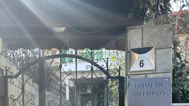 Una entrada tancada amb una placa que diu 'HOME OF OLYMPIOS' i un codi QR.