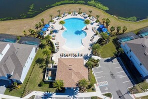 Eine Vogelperspektive auf ein Resort mit einem zentralen Swimmingpool, Liegestühlen und Palmen.