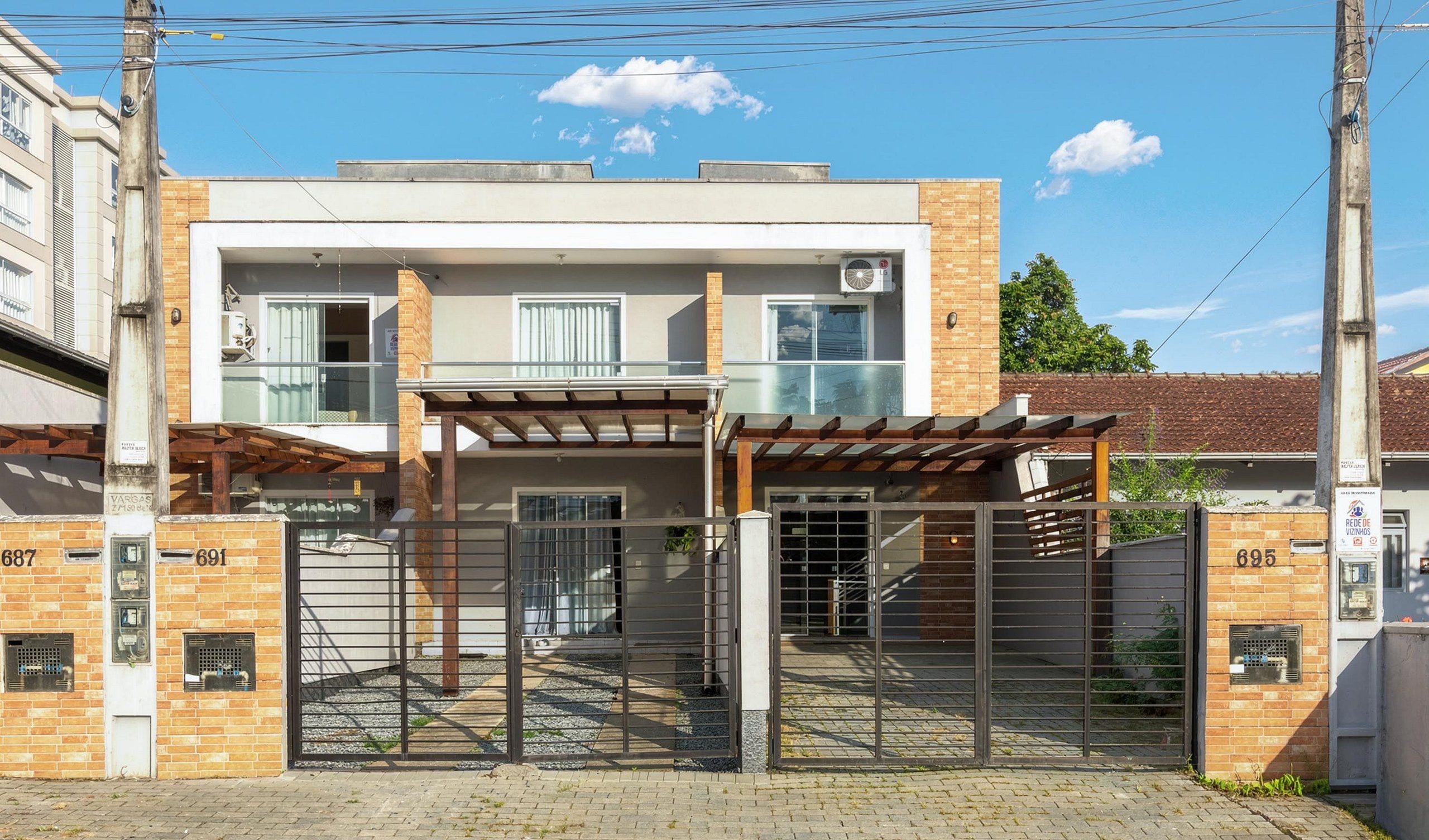 A modern two-story building with a gated entrance, a covered patio, and a visible air conditioning unit.