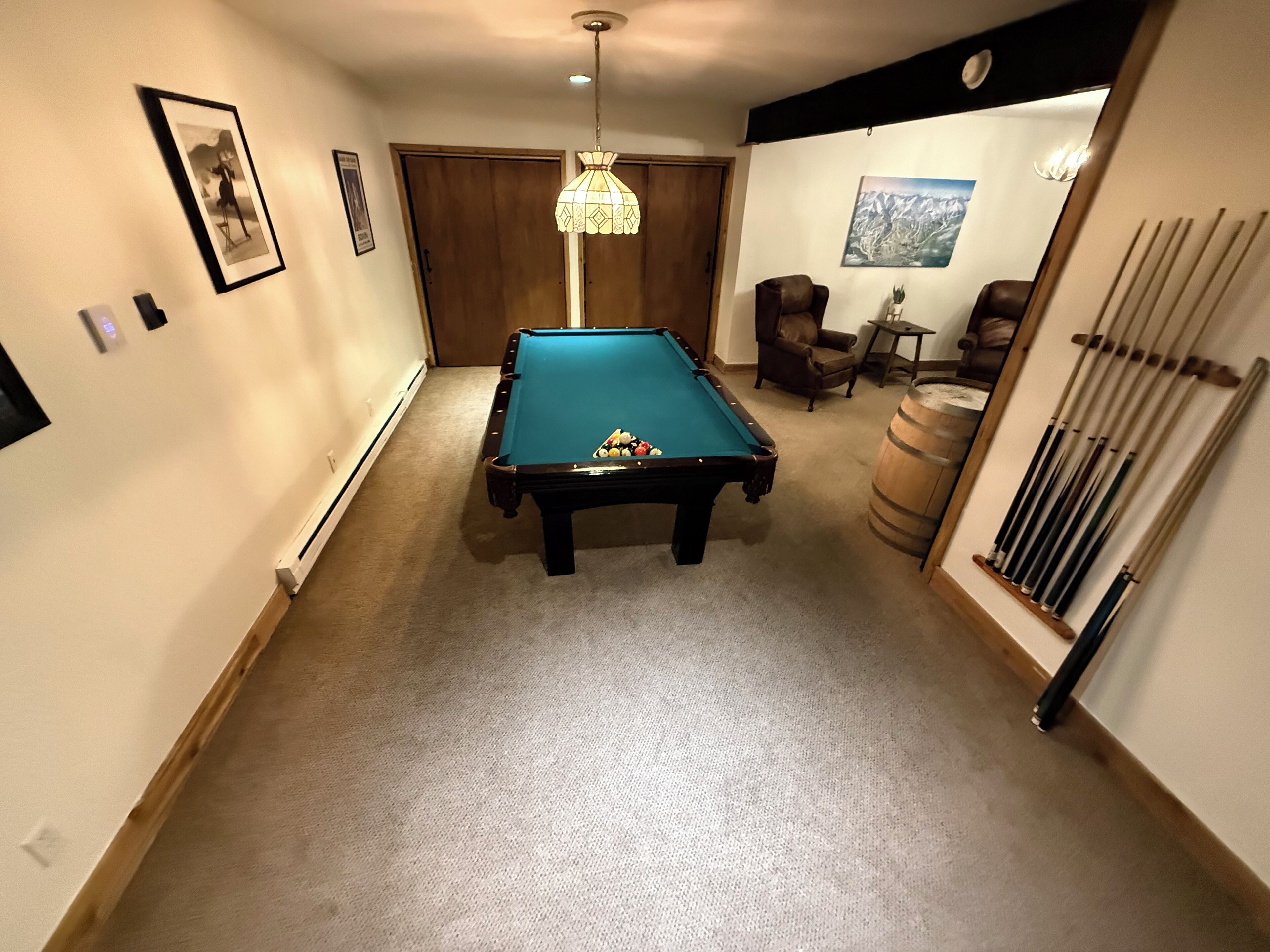 Une table de billard dans une pièce avec une porte en bois, une chaise et un porte-queue fixé au mur.