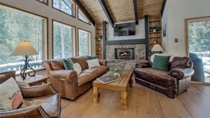 A cozy living room with a fireplace, leather sofas, wooden coffee table, and large windows. - 4-bedroom house with Hottub in charming Breckenridge (Breckenridge)