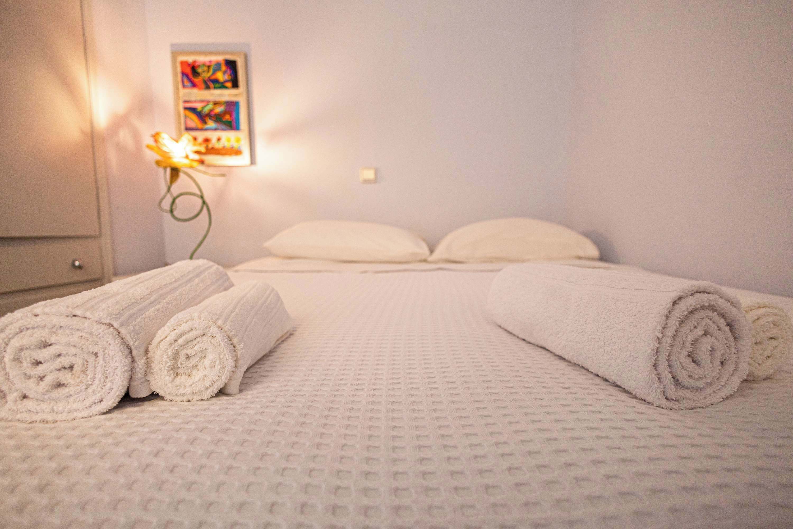 A hotel room with a bed, two pillows, and rolled towels on the bed.