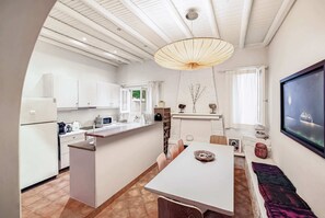 Eine moderne Küche mit weißen Schränken, ein Essbereich mit Tisch und Stühlen und ein großes Fenster mit Vorhängen.