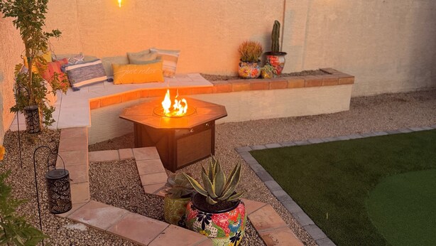Een terras met vuurkorf, zitplaatsen, potplanten en een verzorgd gazon.