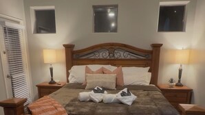 Een slaapkamer met een houten bed, twee nachtkastjes, een plafondventilator en twee ramen.