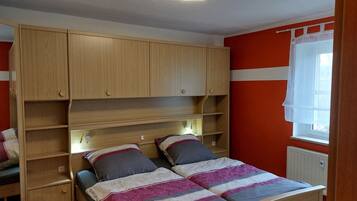 Ein Schlafzimmer mit einem Bett, einem Holzschrank, Regalen und einem Fenster mit Vorhängen.