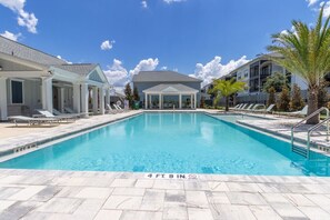 A swimming pool with lounge chairs and a covered area, surrounded by buildings and palm trees. - Seagate at Clara Beach Getaway | 3 Bedrooms • Sleeps 6 (Panama City Beach)