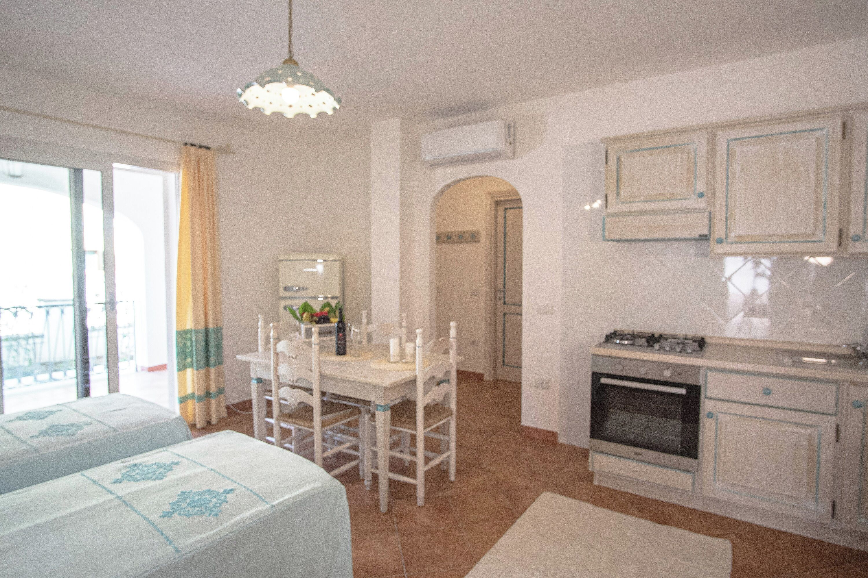 Una habitación con mesa de comedor, sillas, área de cocina con armarios y un balcón.