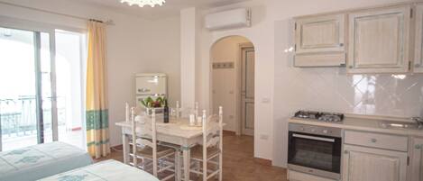 Una habitación con mesa de comedor, sillas, área de cocina con armarios y un balcón.