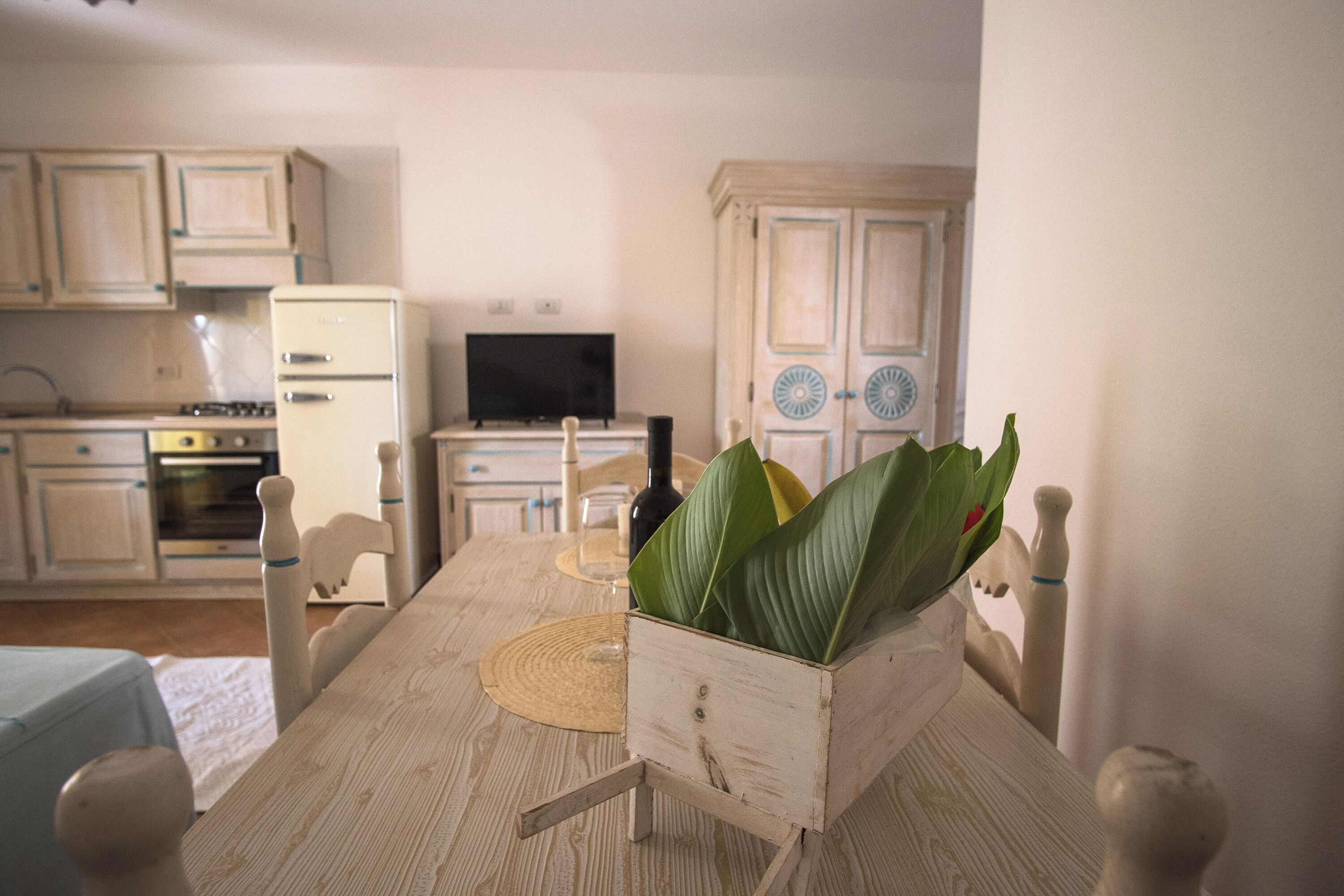 Una mesa de comedor con sillas, un televisor y una cocina al fondo.