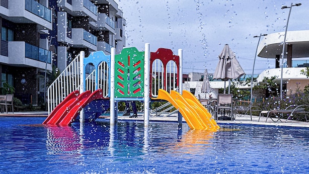 A swimming pool with colorful slides and a modern building in the background. - Flat em resort - Várias Piscinas (Ipojuca)