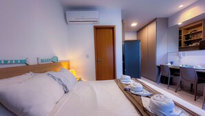 A hotel room with a bed, a desk, a refrigerator, and a dining area. - Flat em resort - Várias Piscinas (Ipojuca)