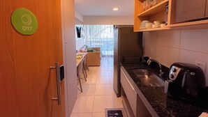 A narrow kitchen with a dining area, a coffee machine, and a TV mounted on the wall. - Flat em resort - Várias Piscinas (Ipojuca)
