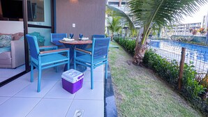 A patio with blue wicker furniture, a small table with glasses, and a purple cooler. - Flat em resort - Várias Piscinas (Ipojuca)