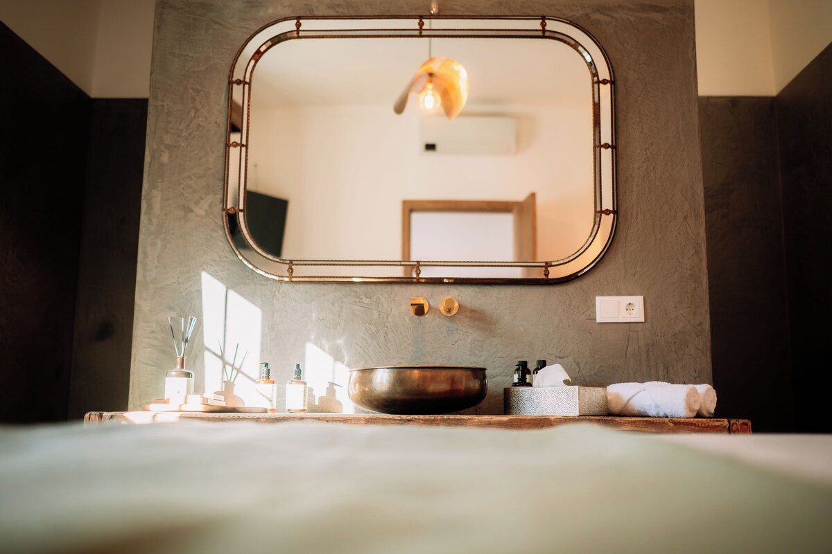 A bathroom with a large mirror, a sink with a bowl, a towel, and a window providing natural light.