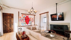 A living room with a sofa, a chandelier, a fireplace, and a TV mounted on the wall. - Herdade dos Moreiros (Arronches)