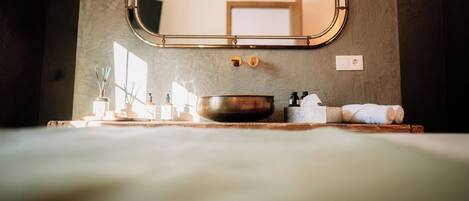 A bathroom with a large mirror, a sink with a bowl, a towel, and a window providing natural light.