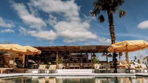 A poolside area with lounge chairs, umbrellas, and a palm tree. - Herdade dos Moreiros (Arronches)