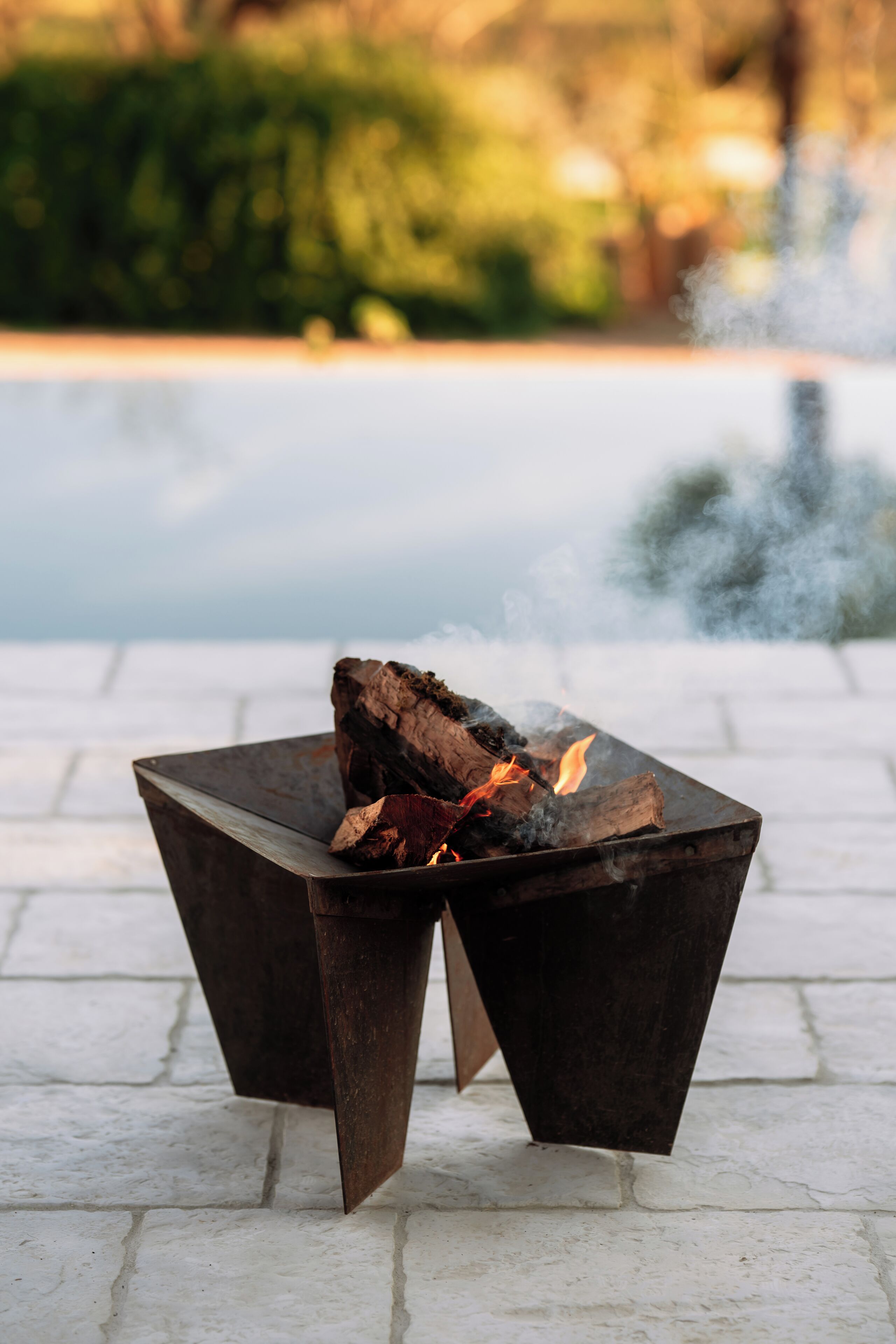 A metal fire table with a fire burning on a paved surface.