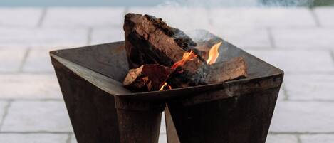 A metal fire table with a fire burning on a paved surface.