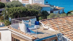 Ett bostadsområde med tak som är täckta av terrakottafärgade tegelpannor, en balkong med kuddar och utsikt över havet.