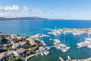 An aerial view of a coastal town with a marina filled with boats, surrounded by residential buildings and a clear blue sky. - Darsena View - loft with panoramic harbor views (Olbia)