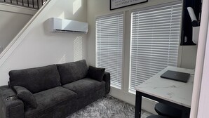 Un espace de vie moderne avec un canapé gris, un tapis à motifs, une table blanche sur laquelle se trouve un ordinateur portable et un escalier.