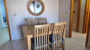 A dining area with a wooden table and chairs, a round mirror on the wall, and a door leading to another room. - Holidays in Playa Golf 2 (Orihuela)