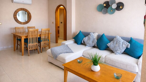 A living room with a sofa, coffee table, and dining area with chairs and a table. - Holidays in Playa Golf 2 (Orihuela)