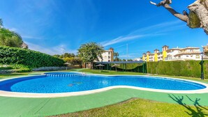 A swimming pool with a curved edge, surrounded by a green lawn and a hedge. - Holidays in Playa Golf 2 (Orihuela)