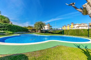 A swimming pool with a curved edge, surrounded by a green lawn and a hedge. - Holidays in Playa Golf 2 (Orihuela)