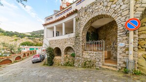Edifici de pedra amb un balcó, senyal de prohibició d'aparcament i un cotxe estacionat a un carrer empedrat.