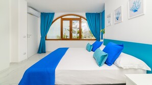 Un dormitori amb llit, cortines, una finestra i quadres emmarcats a la paret.
