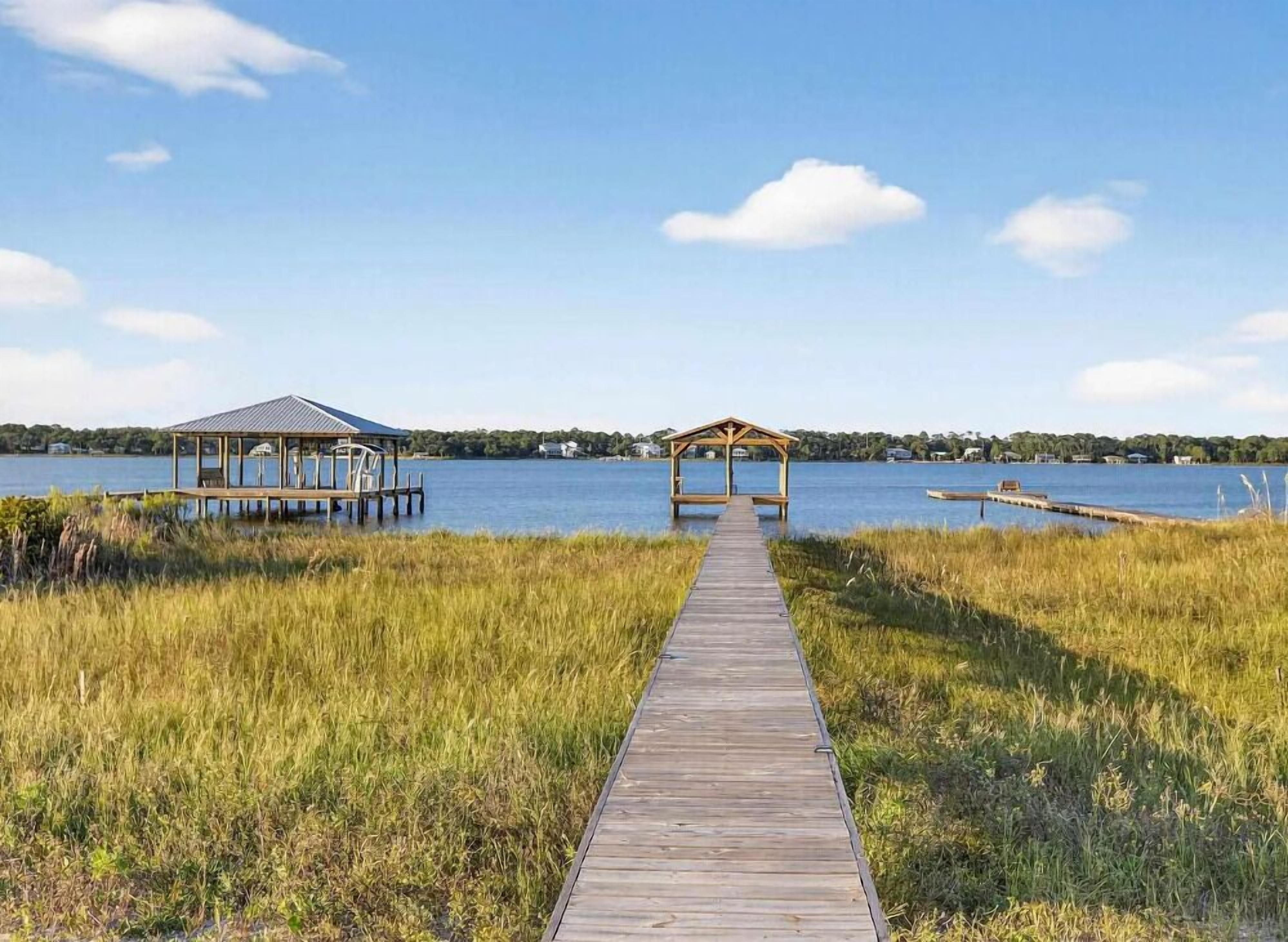 Un muelle de madera que conduce a dos gazebos sobre el agua, bajo un cielo despejado.