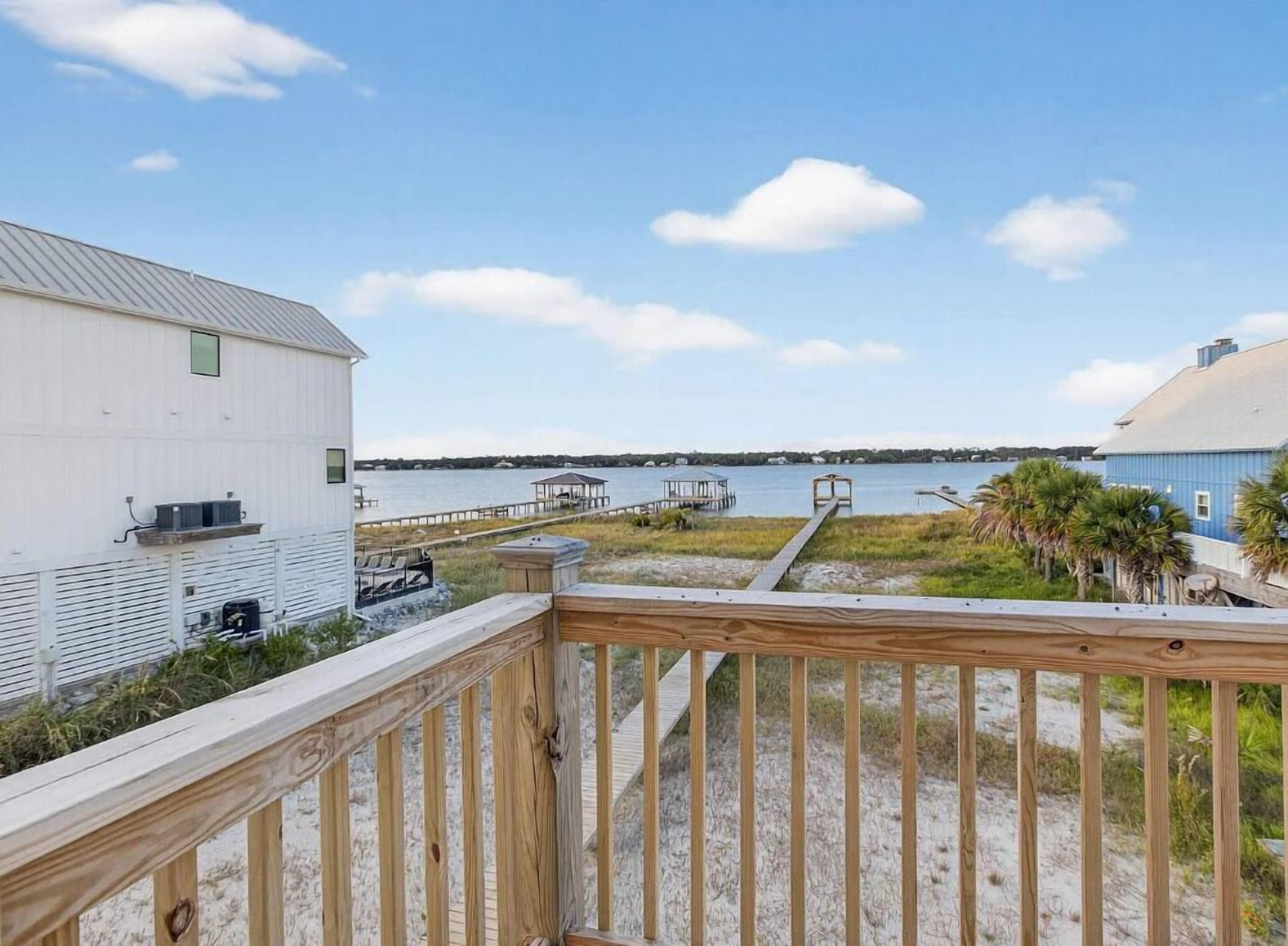 A beachside property with a wooden deck, a white building, and a blue building, overlooking a calm body of water.