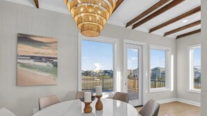 A spacious room with a round table, chairs, a chandelier, large windows, and a painting. - Salt Water Heals Everything (Gulf Shores)